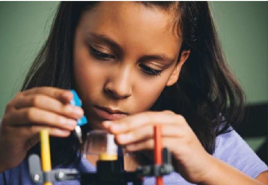 A teacher guiding three students through a robotics project at a table